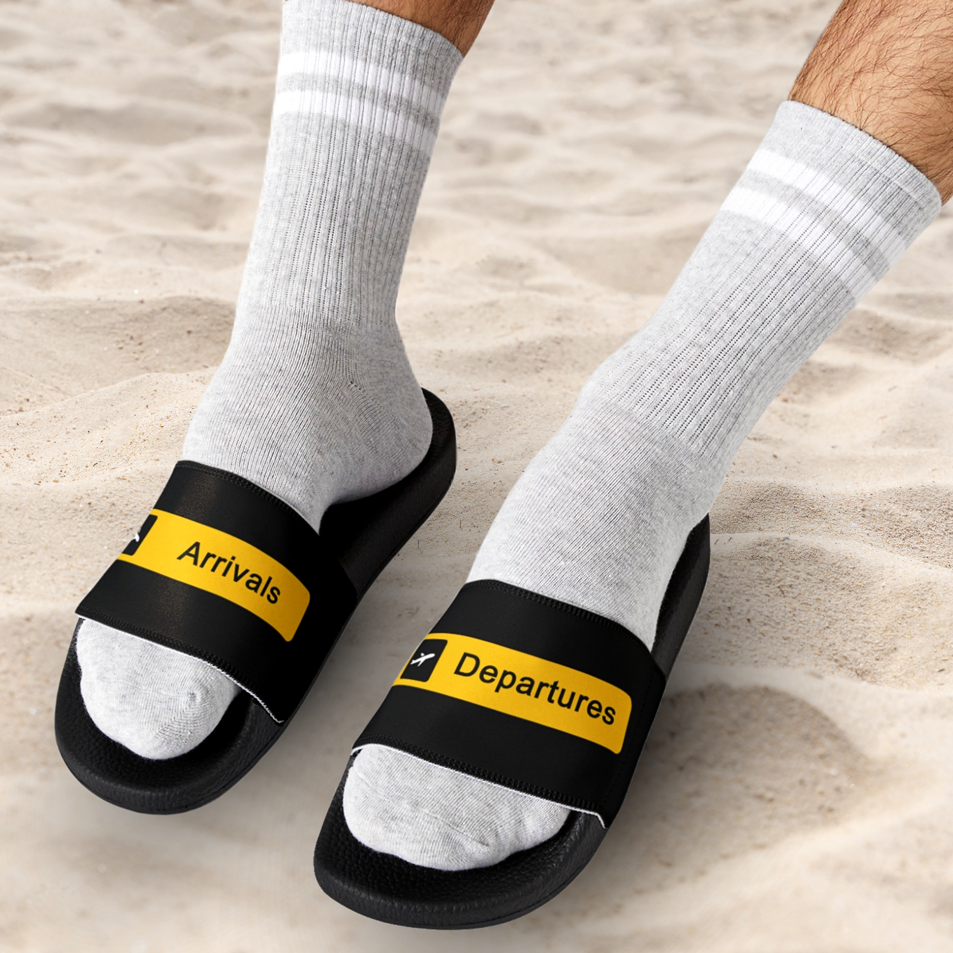 Man at the beach wearing black Slides with the words Arrivals and Departures on each foot